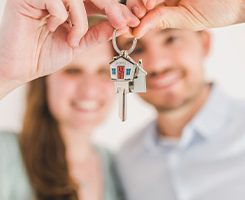 Photo of a young couple holding up a house shaped key ring with a key on it