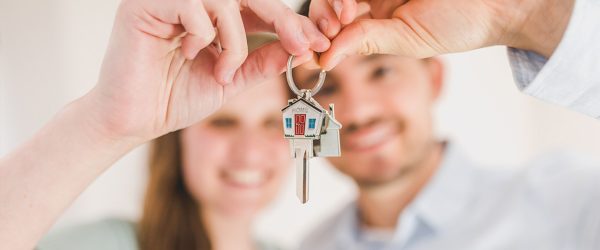 Photo of a young couple holding up a house shaped key ring with a key on it