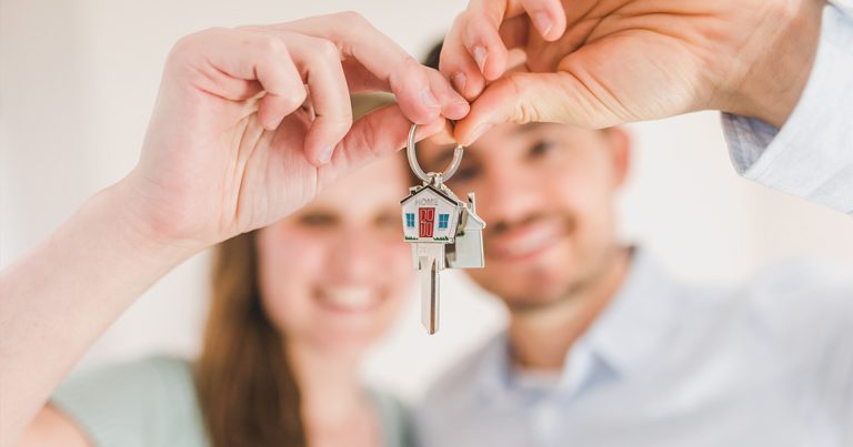 Photo of a young couple holding up a house shaped key ring with a key on it