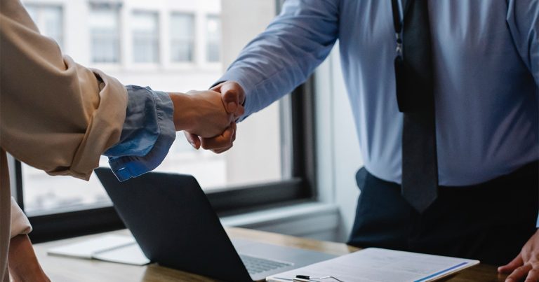 People shake hands over a laptop