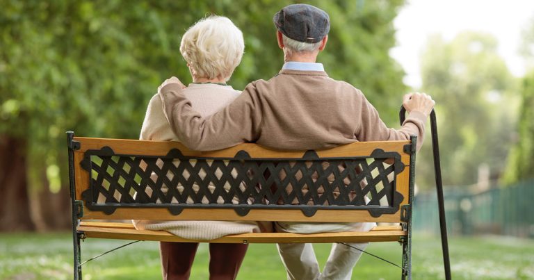 an older couple sitting on a bench in a park.